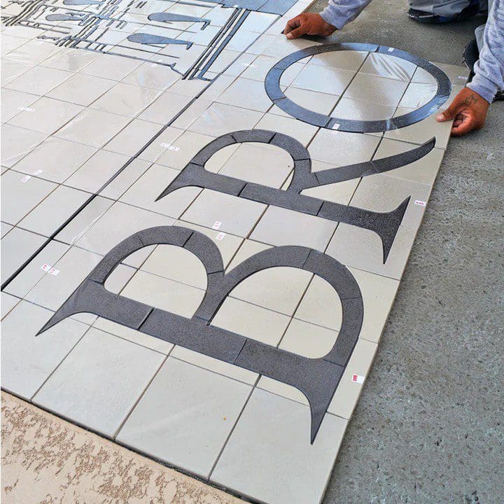 Person installing large letter tiles spelling 'BRO' on a floor.