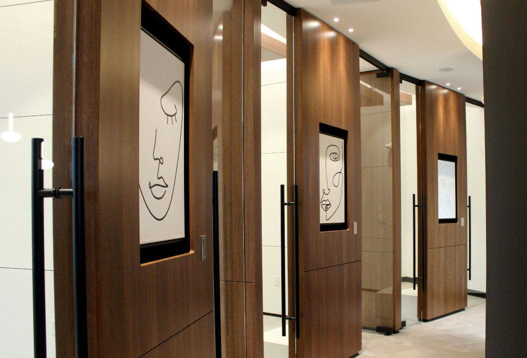 Modern restroom stalls with artistic face line drawings on wooden doors.