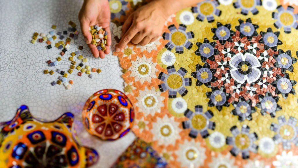 Hands arranging colorful mosaic tiles in intricate patterns.