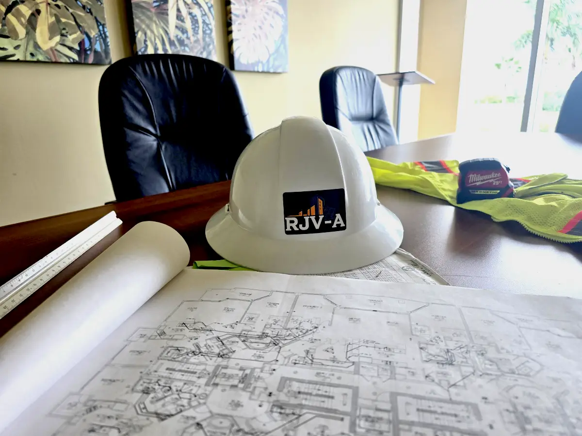 A construction helmet and blueprints on a table in an office.