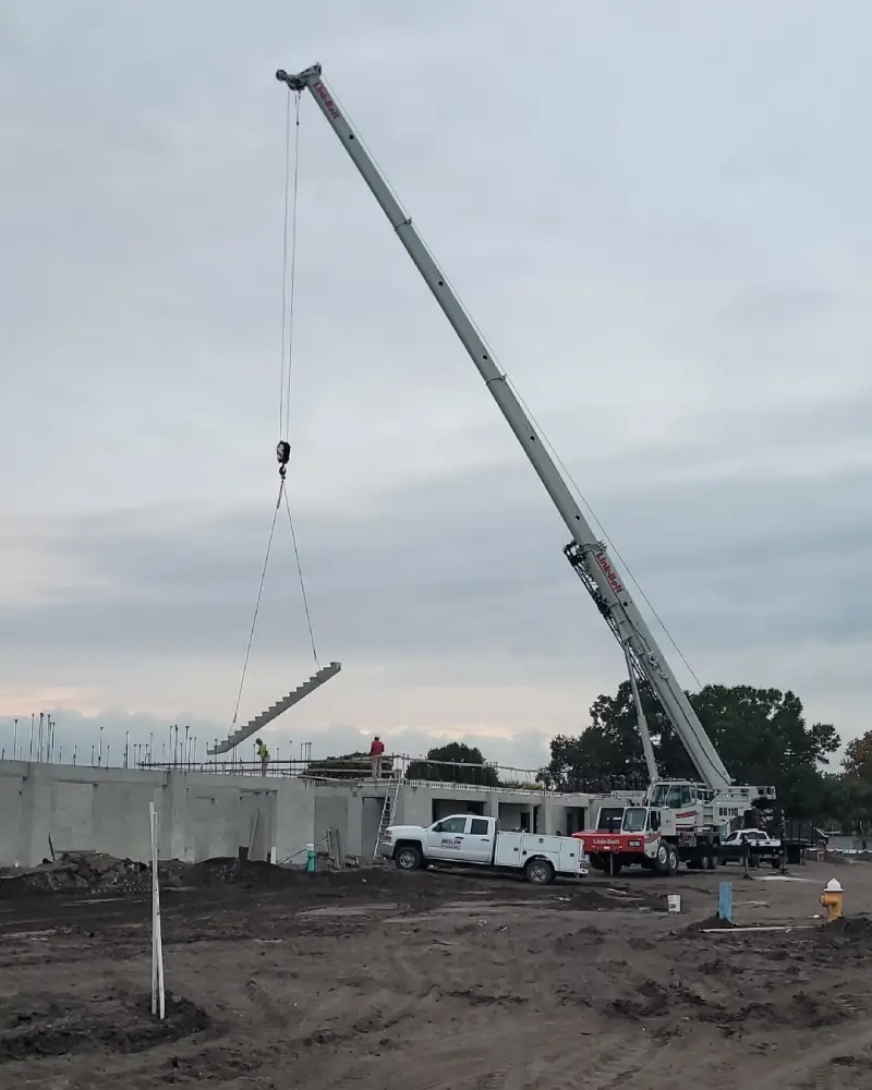 A crane lifting a long metal beam at a construction site during dusk.