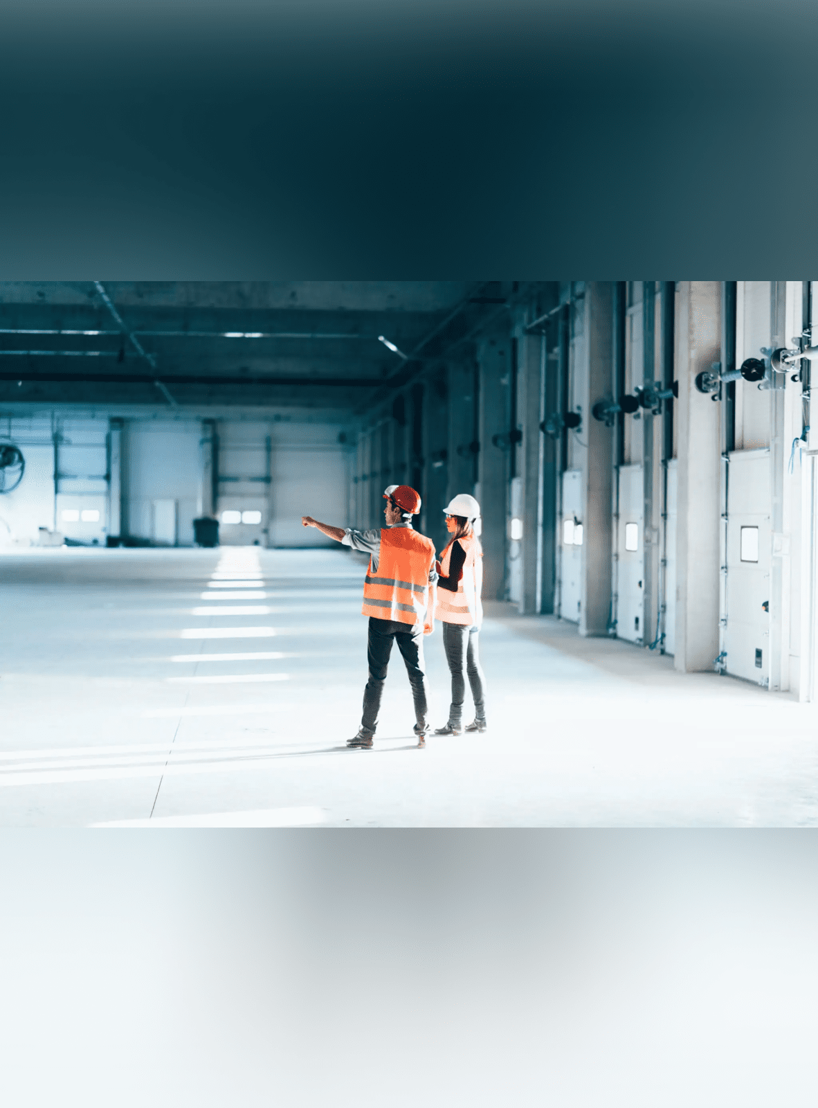 Two construction workers discussing plans in a spacious warehouse.