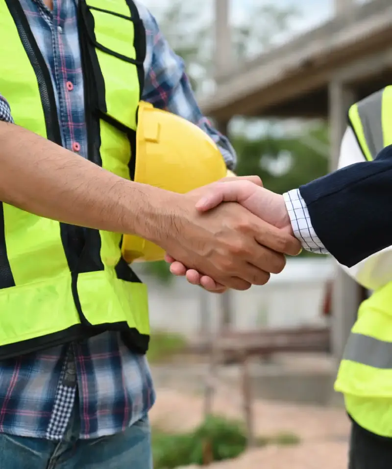 Two professionals shaking hands at a construction site, symbolizing partnership.