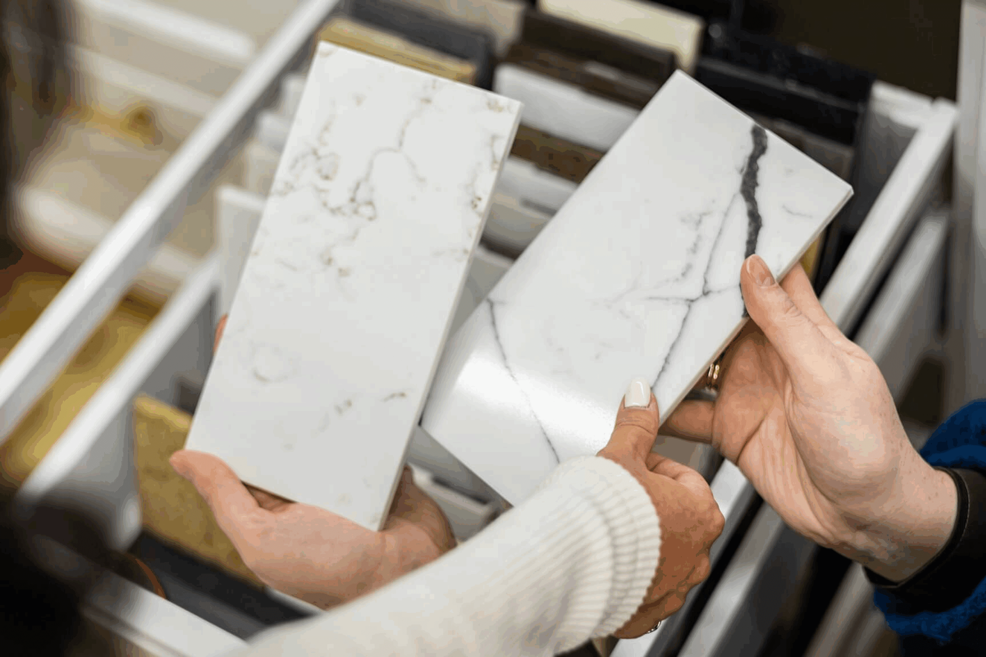 Hands holding marble tile samples with different veining patterns.